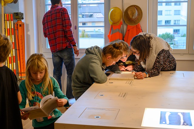 Besucher beugen sich über Tisch und lesen in Büchern.