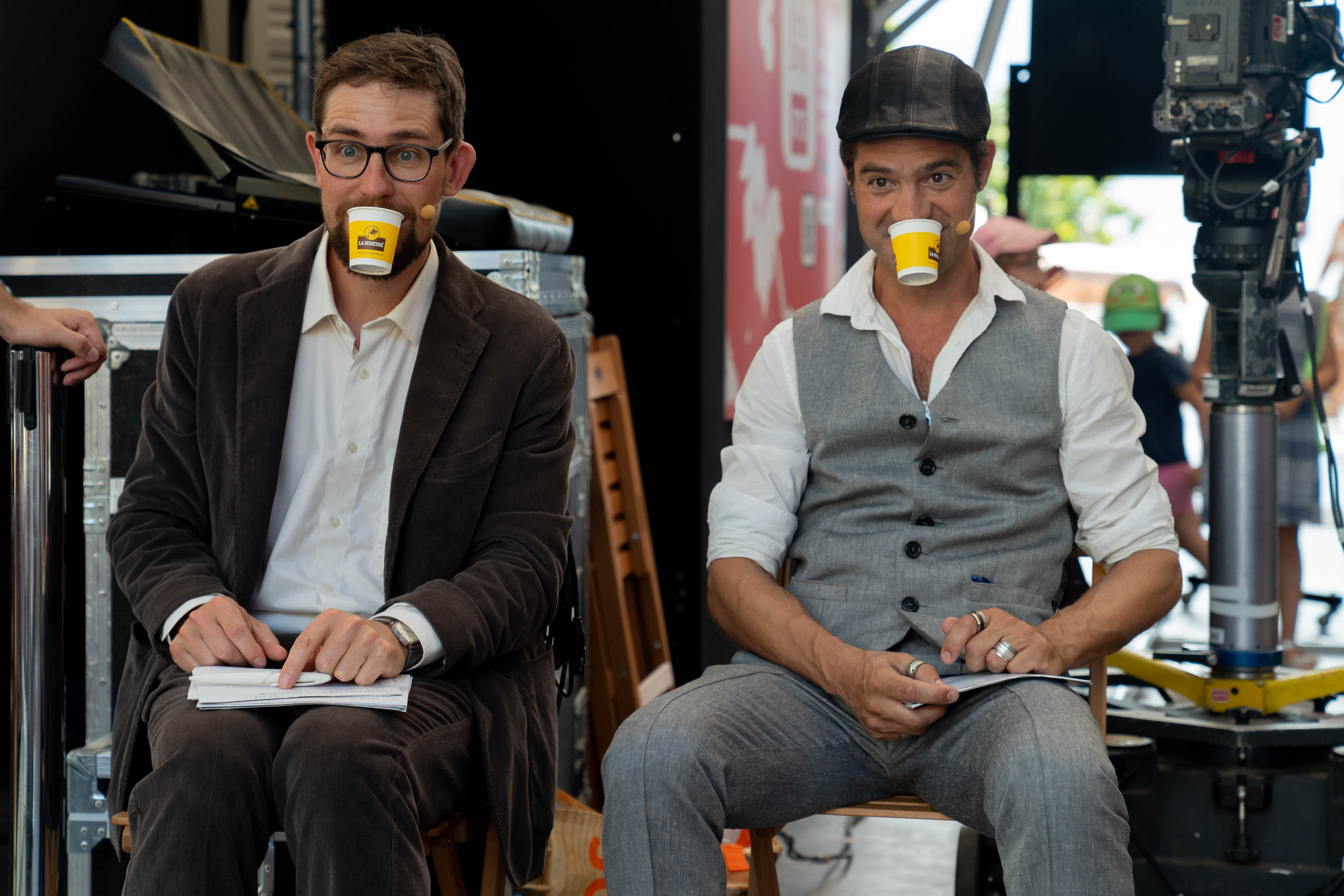 Das Kabarettduo Strohmann-Kauz sitzt auf Stühlen mit Bechern im Mund.