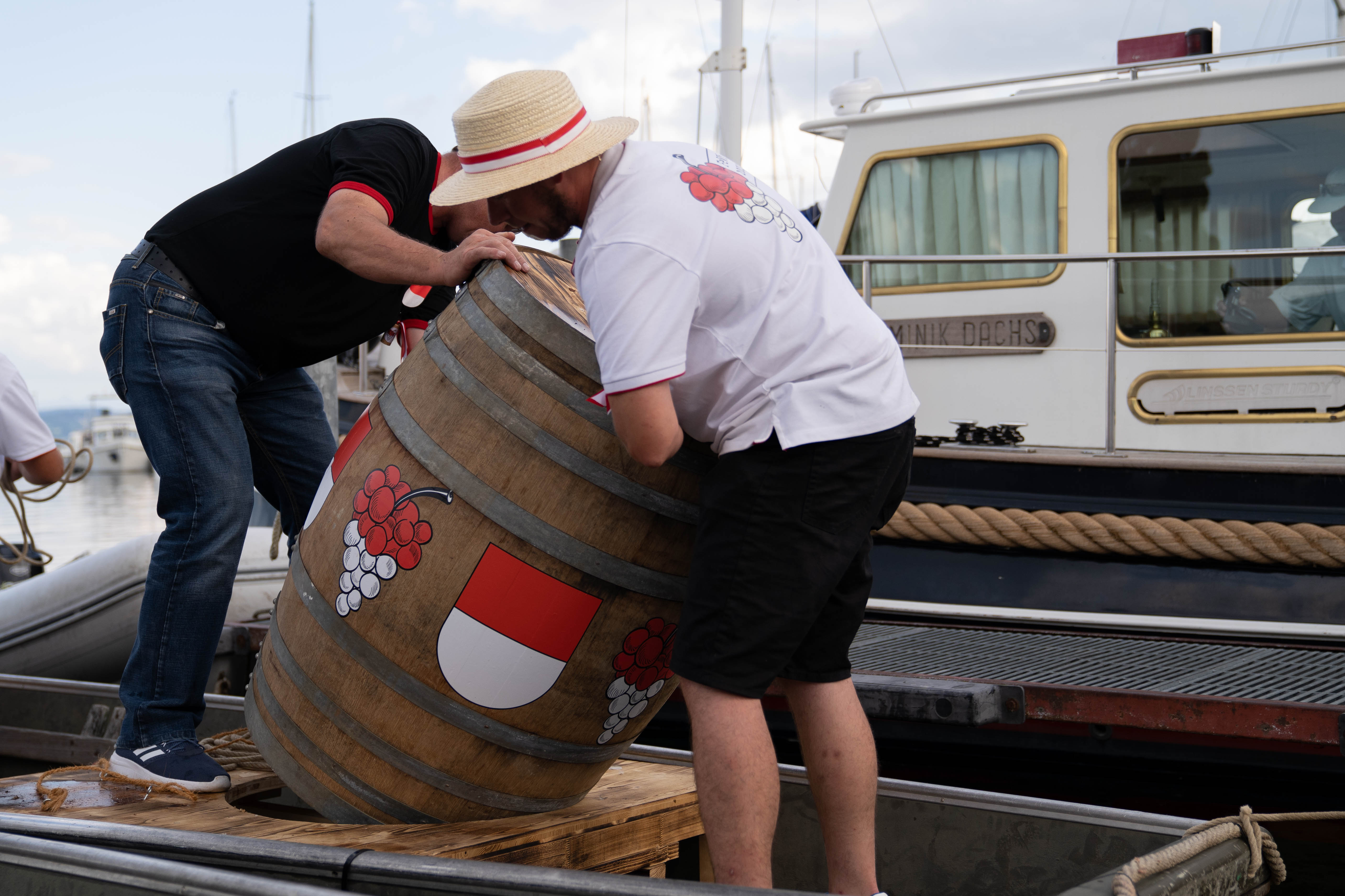 Zwei Männer tragen ein Weinfass ab einem Schiff.