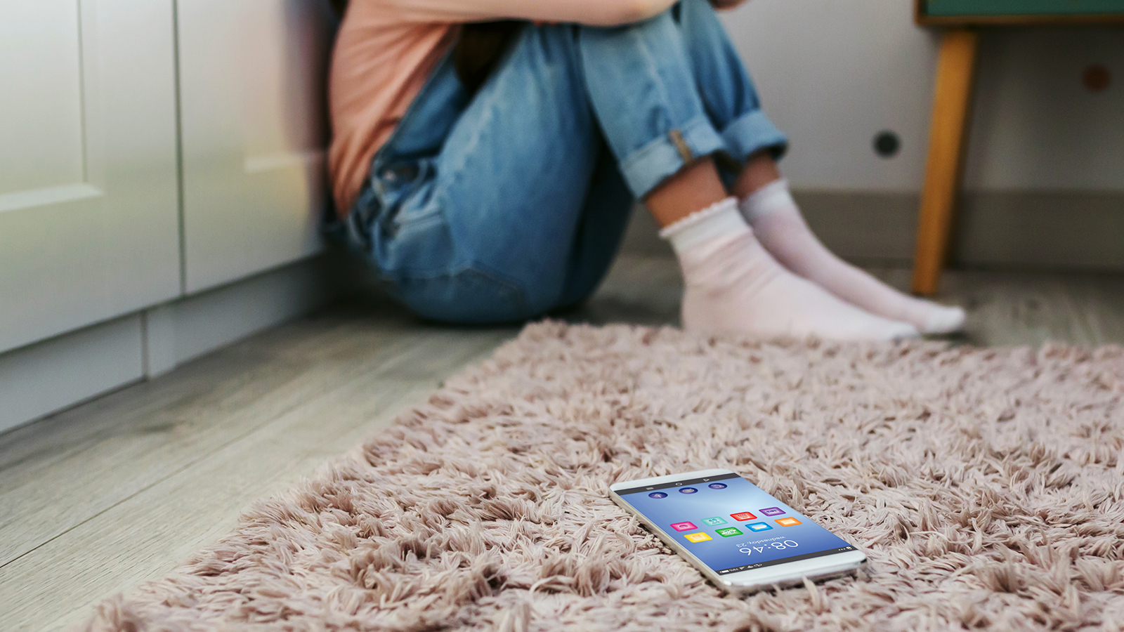 Junge Person kauert auf dem Boden, ein Smartphone liegt daneben