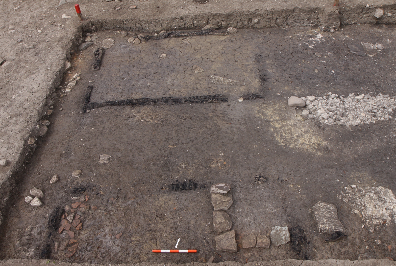 Im Boden sind die verkohlten Schwellbalken eines oder mehrerer Holzgebäude zu erkennen. Im Vordergrund rechts eine rechtwinklig angeordnete Steinsetzung, die als Unterlage für einen Kachelofen gedient haben könnte.